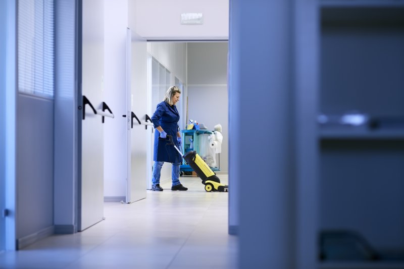 Reinigungskraft in dunkelblauem cleanteam-Shirt reinigt Sanitäranlage in einem Verwaltungsgebäude